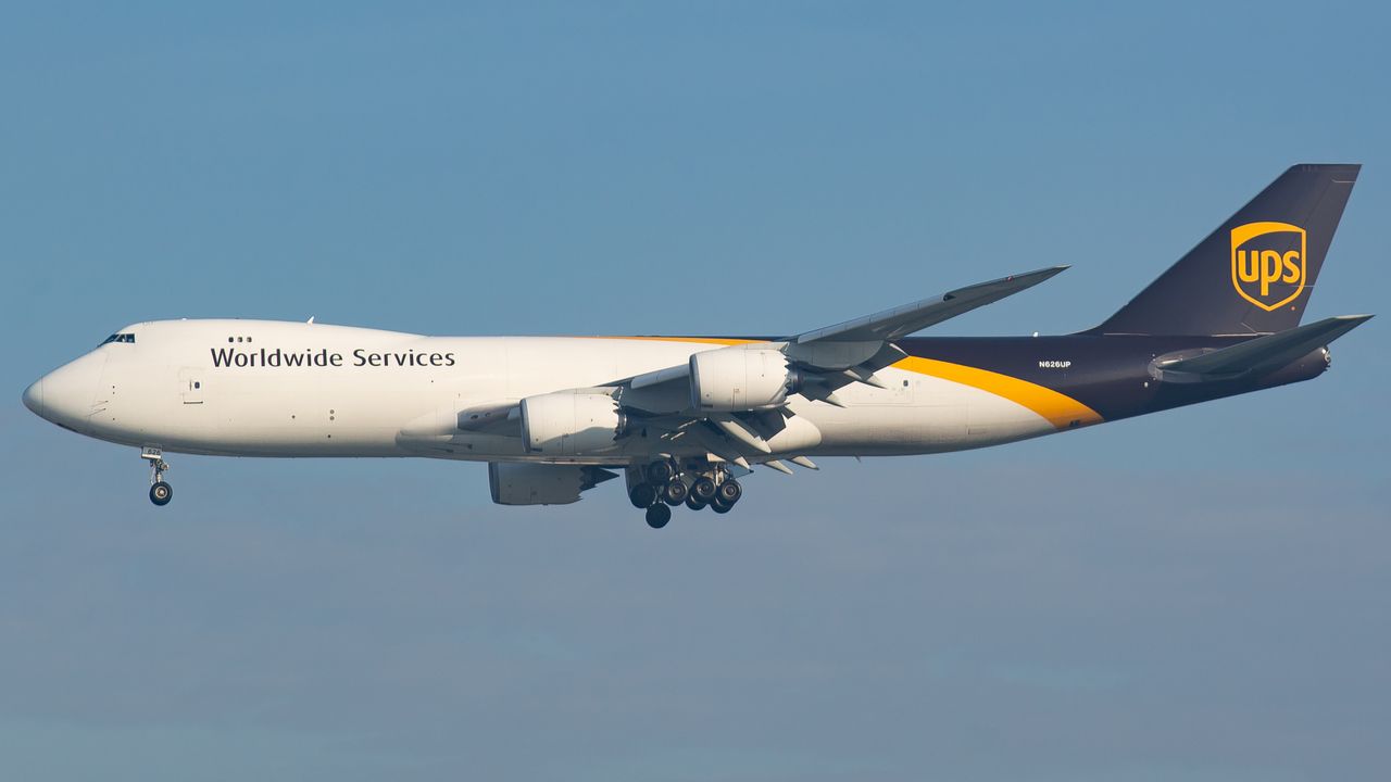 UPS cargo plane in flight against clear blue sky, showcasing delivery services.
