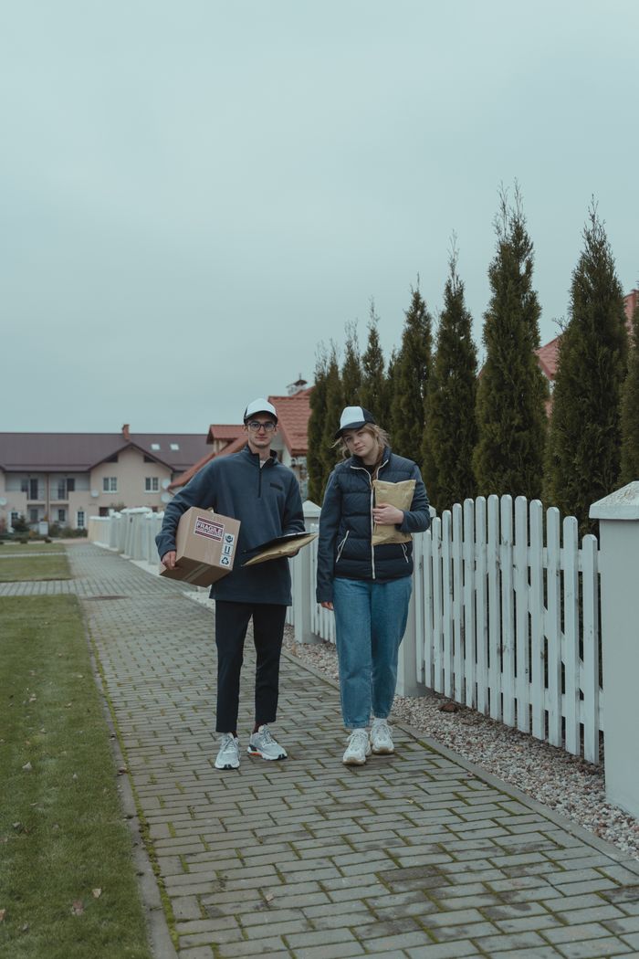 Two couriers delivering packages in a suburban neighborhood on a cloudy day.